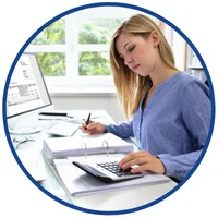 Kurs podatkowy dla samodzielnych księgowych – kobieta notuje przy biurku z kalkulatorem, segregatorem i monitorem